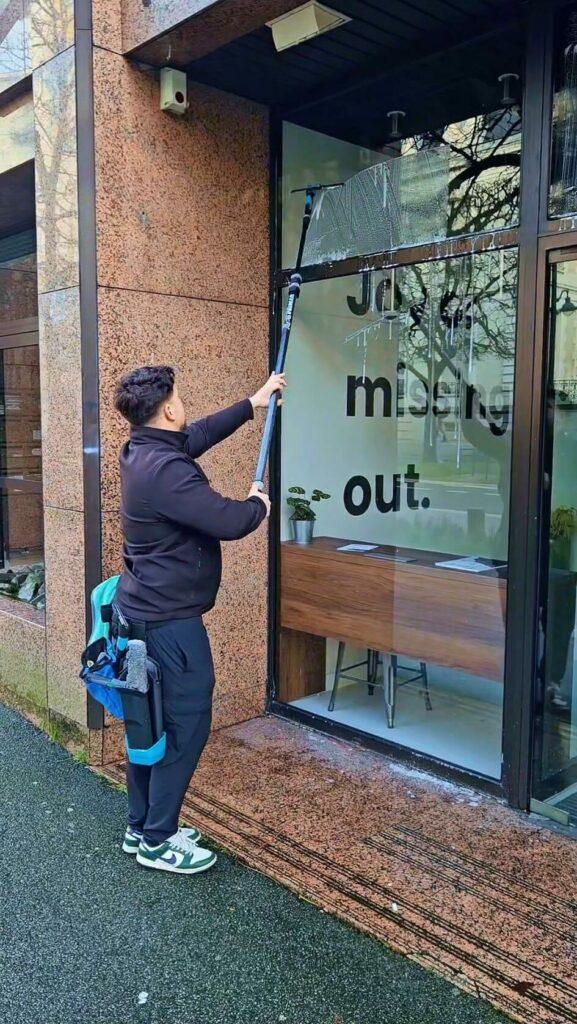 Laveur de vitres Glaz Services nettoyant la vitrine d'un commerce à Rennes avec une perche